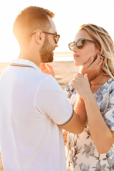 Foto de casal sedutor romântico sorrindo e acariciando um ao outro enquanto caminhava na praia ensolarada — Fotografia de Stock