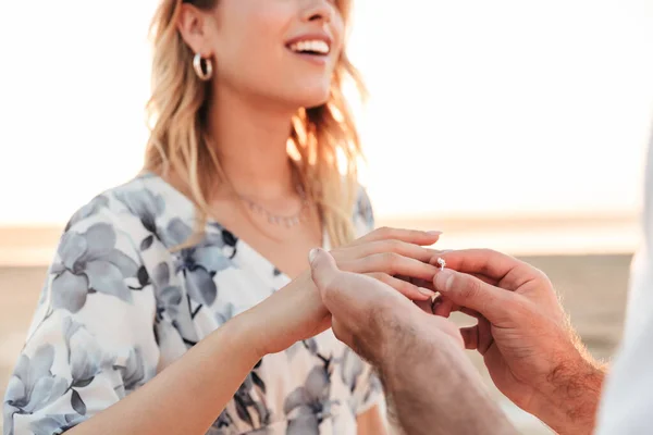 Gesneden foto van jonge man zetten verlovingsring om de vinger van de vrouw tijdens het lopen op het strand — Stockfoto