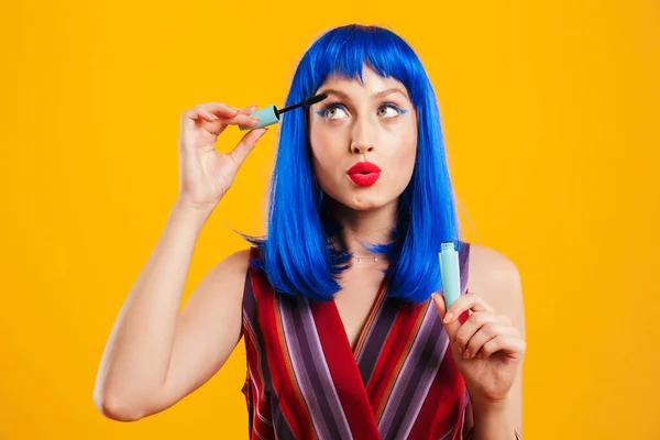 Porträtt av ung vacker kvinna bär blå peruk tittar uppåt och tillämpa mascara — Stockfoto