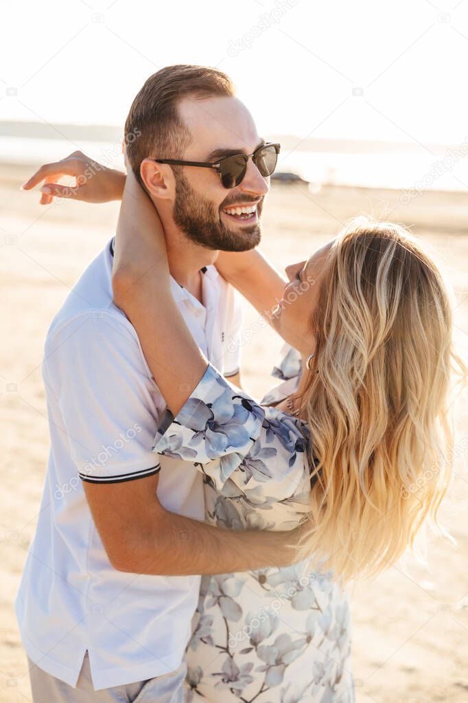 Photo of attractive happy couple laughing and hugging while walking on sunny beach