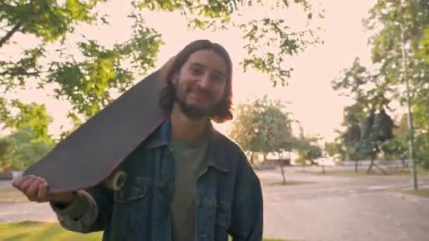 Bonito Jovem Barbudo Jaqueta Ganga Sorrindo Segurando Skate Seu Ombro — Vídeo de Stock