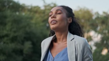 Yorgun ve yorgun bir Afrikalı iş kadını parkta dikilirken kolye takıyor.