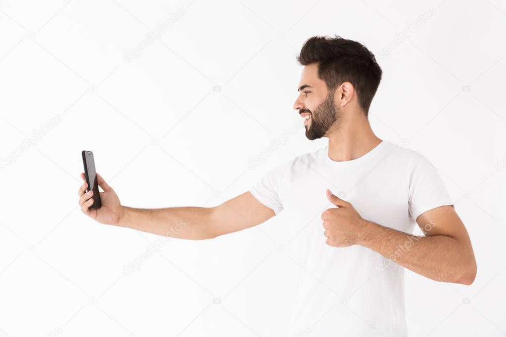 Image of handsome joyful man showing thumb up and taking selfie photo on cellphone