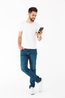 Çekici bir gencin cep telefonuyla gülümseyen ve daktilo yazan tam boy görüntüsü.