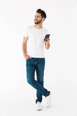 Çekici, gülümseyen bir adamın tam boy görüntüsü yana bakıyor ve cep telefonunda yazıyor.