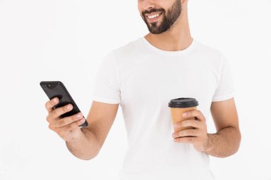 Kahve içen ve cep telefonu kullanan yakışıklı, neşeli bir adamın görüntüsü.