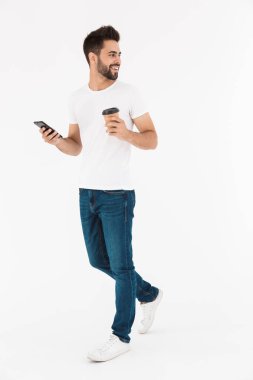 Neşeli, güler yüzlü, kahve içen ve cep telefonuyla yazan bir adamın tam boy görüntüsü.