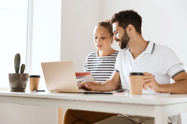 Concentrato giovane coppia amorevole amici uomo e donna seduti al tavolo al chiuso utilizzando computer portatile lettura libro di studio . — Foto Stock