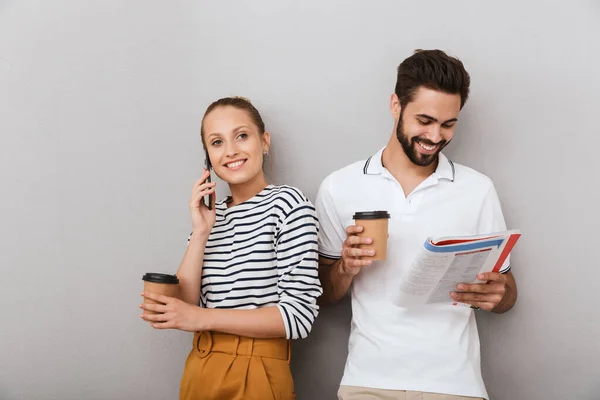 Boldog fiatal elégedett szerető pár barátok férfi és nő beltérben elszigetelt szürke háttér beszél mobiltelefon gazdaság copybook. — Stock Fotó