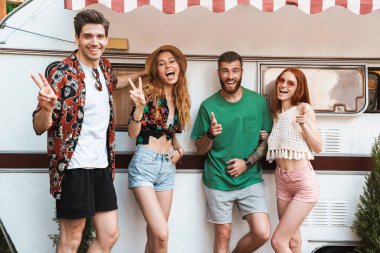 Bir grup neşeli gülen arkadaş karavanın önünde dikiliyorlar.