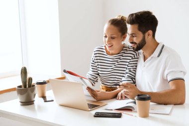 İyimser, mutlu, mutlu, genç, sevgi dolu iki arkadaş. Erkek ve kadın, kapalı bir masada dizüstü bilgisayar okuma kitabı kullanarak oturuyor..