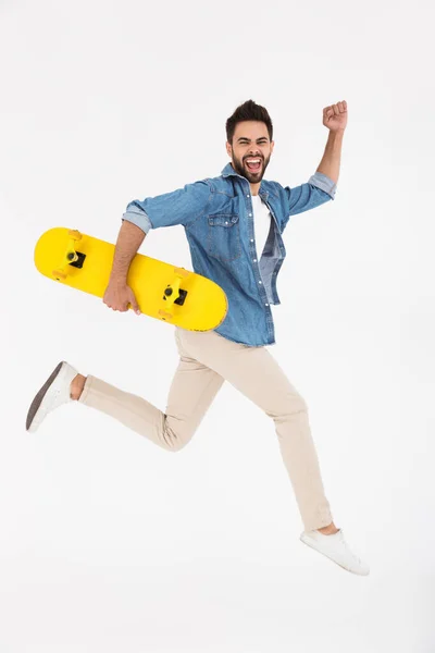 Imagen completa del hombre feliz y excitado corriendo y sosteniendo el monopatín — Foto de Stock