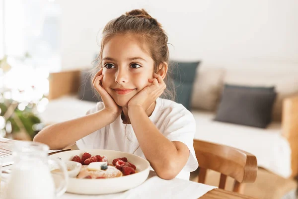 Портрет чарівної маленької дівчинки, що сидить за столом у яскравому наборі — стокове фото