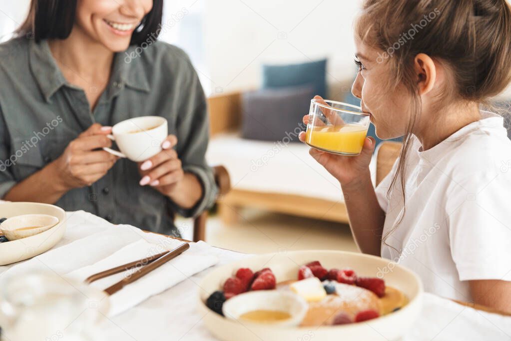Image of smiling family mother and little daughter having breakf