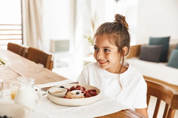 Портрет щасливої маленької дівчинки, що сидить за столом на світлій кухні — стокове фото