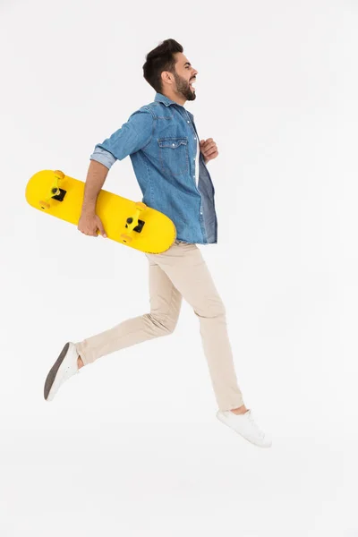 Full length image of unshaven excited man running and holding skateboard — Stock Photo, Image