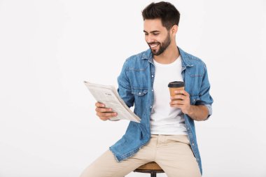 Yakışıklı, gülümseyen bir adam kahve içerken ve sandalyede otururken gazete okurken.