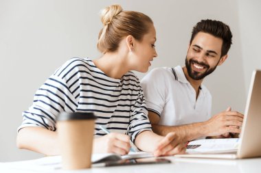 Memnun genç çift arkadaşları erkek ve kadın kapalı bir masada oturuyor dizüstü bilgisayarla not defteri yazarak ders çalışıyorlar..