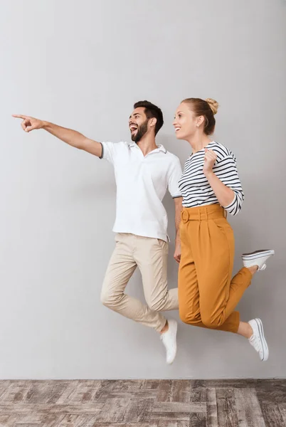 Emotioneel verrast liefdevol paar vrienden man en vrouw springen binnen geïsoleerd over grijze achtergrond wijzend. — Stockfoto