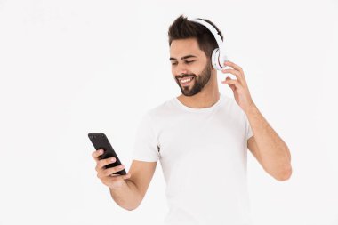 Cep telefonu ve kulaklıkla müzik dinleyen traşsız, gülümseyen bir adam görüntüsü