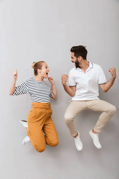 Emotional glücklich liebende Paar Freunde Mann und Frau springen im Haus isoliert über grauen Hintergrund machen Siegergeste. — Stockfoto