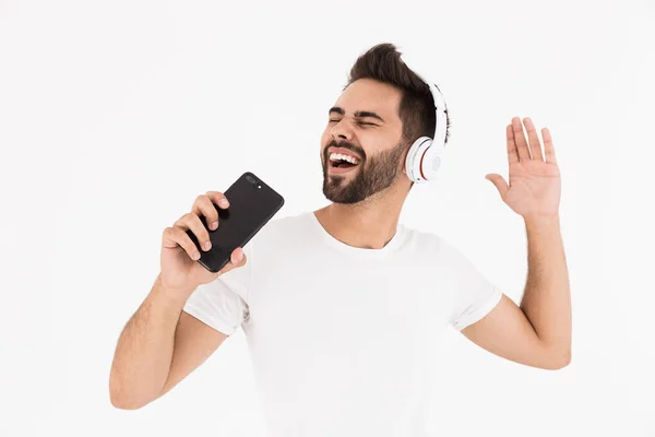 Imagen del hombre sonriente sin afeitar cantando mientras escucha música en el teléfono celular y los auriculares —  Fotos de Stock