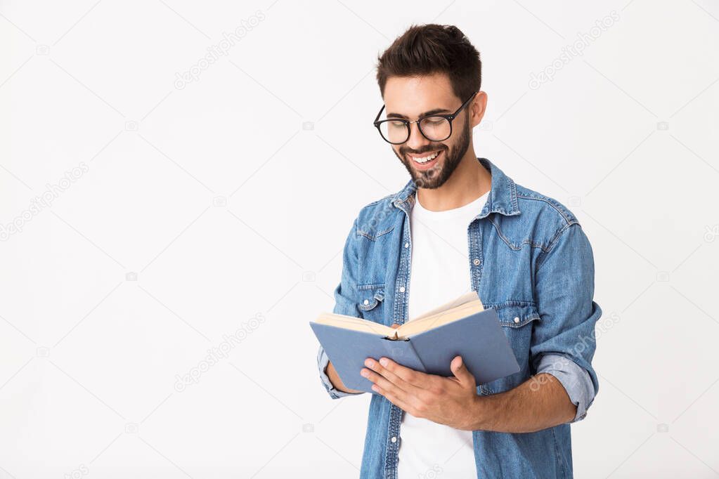 Image of young happy man wearing eyeglasses reading book and smiling