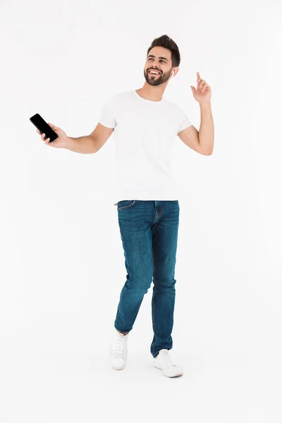 Image pleine longueur d'un homme souriant joyeux écoutant de la musique sur son téléphone portable et son oreillette tout en dansant — Photo