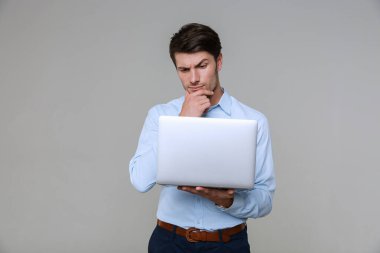 Ofis kıyafetleri içinde dizüstü bilgisayarlı düşünceli bir iş adamı resmi.