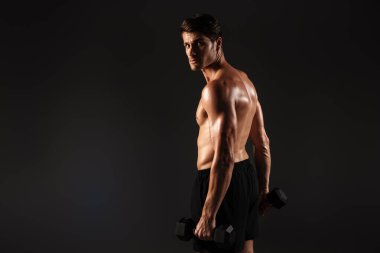 Elinde dambıllarla siyah duvar arkasında yalnız poz veren konsantre olmuş yakışıklı genç ve güçlü bir sporcu..