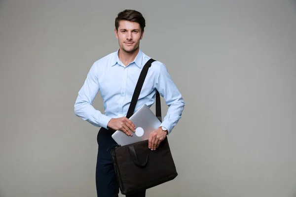 Obrázek pohledného podnikatele, jak dává notebook do tašky — Stock fotografie