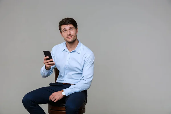 Retrato de hombre de negocios guapo sosteniendo el teléfono celular mientras está sentado — Foto de Stock
