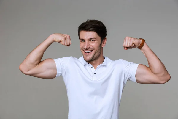 Afbeelding van positieve brunette man glimlachen en tonen zijn biceps — Stockfoto