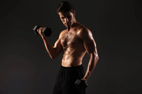 Concentrado bonito jovem forte desportista posando isolado sobre preto parede fundo segurando halteres . — Fotografia de Stock