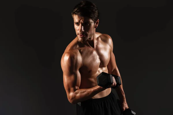 Concentrated handsome young strong sportsman posing isolated over black wall background holding dumbbells. — Stock Photo, Image