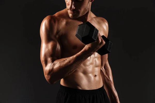 Concentrado guapo joven deportista fuerte posando aislado sobre fondo negro de la pared sosteniendo pesas . —  Fotos de Stock