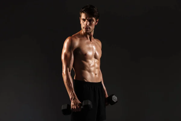 Concentrado guapo joven deportista fuerte posando aislado sobre fondo negro de la pared sosteniendo pesas . —  Fotos de Stock