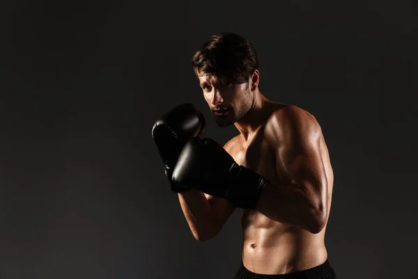 Guapo joven deportista fuerte boxeador en guantes hacer ejercicios de boxeo aislado sobre fondo negro de la pared . — Foto de Stock