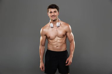 Neşeli, iyimser, yakışıklı, güçlü sporcu. Gri duvar arka planında izole edilmiş, kulaklıkları boynunda..