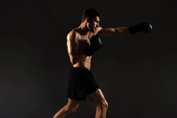 Guapo joven deportista fuerte boxeador en guantes hacer ejercicios de boxeo aislado sobre fondo negro de la pared . — Foto de Stock