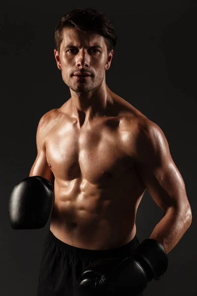 Skoncentrowany silny przystojny młody bokser sportowy w rękawiczkach pozowanie izolowane na tle czarnej ściany. — Zdjęcie stockowe