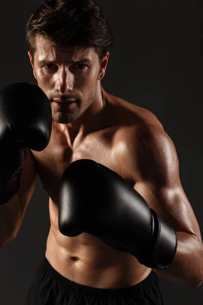 Handsome young strong sportsman boxer in gloves make exercises boxing isolated over black wall background. — Stock Photo, Image