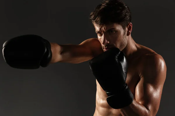 Guapo joven deportista fuerte boxeador en guantes hacer ejercicios de boxeo aislado sobre fondo negro de la pared . — Foto de Stock