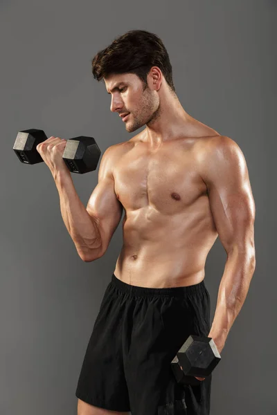 Guapo joven deportista fuerte posando aislado sobre fondo gris de la pared hacer ejercicios con pesas para los brazos . —  Fotos de Stock