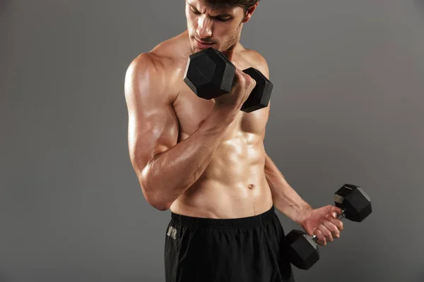 Handsome young strong sportsman posing isolated over grey wall background make exercises with dumbbells for arms. — Stock Photo, Image
