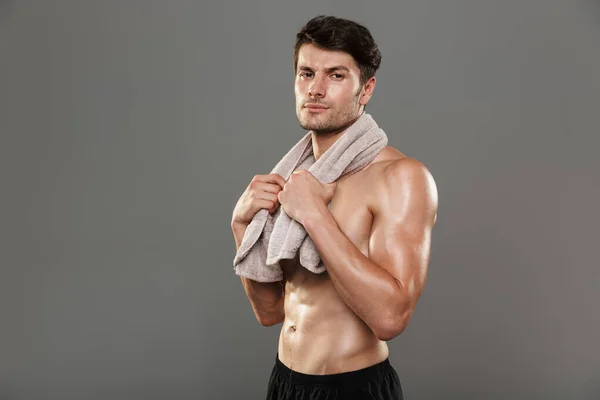 Concentrado sério bonito jovem forte desportista isolado sobre fundo de parede cinza com toalha . — Fotografia de Stock