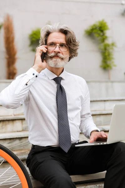 Photo of mature confident businessman using cellphone and laptop — Stock Photo, Image