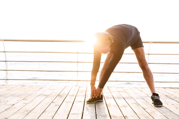 Imagen de un hombre mayor guapo estirando las piernas mientras hace ejercicio — Foto de Stock