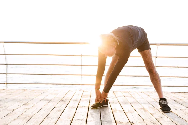 Image of handsome elderly man stretching his legs while working out — Stock Photo, Image