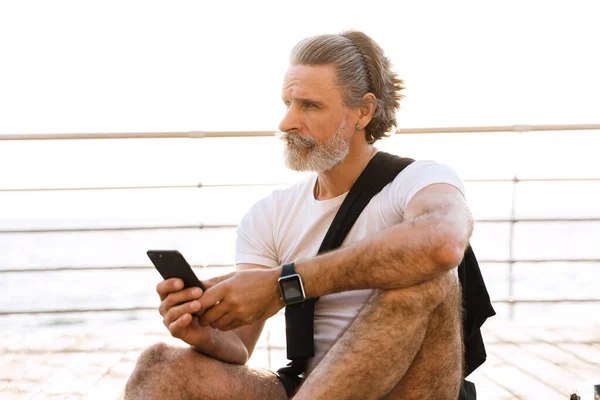 Image of serious elderly man typing on cellphone while sitting — Stock Photo, Image